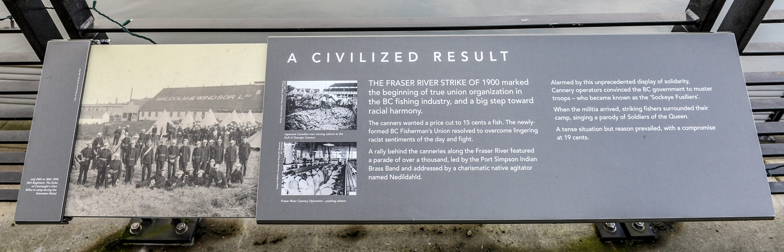 The plaque reads: The fraser river strike of 1900 marked the beginning of true union organization in the BC fishing industry, and a big step toward racial harmony. The canners wanted a price cut to 15 cents a fish. The newly-formed BC Fisherman’s Union resolved to overcome lingering racist sentiments of the day and fight. A rally behind the canneries along the Fraser River featured a parade of over a thousand, led by the Port Simpson Indian Brass Band and addressed by a charismatic native agitator named Nedddiahl. Alarmed by this unprecedented display of solidarity, cannery operators convinced the BC government to muster troops – who became known as the “Sockeye Fusiliers”. When the militia arrived, striking fishers surrounded their camp, singing a parody of Soldiers of the Queen. A tense situation, but reason prevailed, with a compromise at 19 cents.