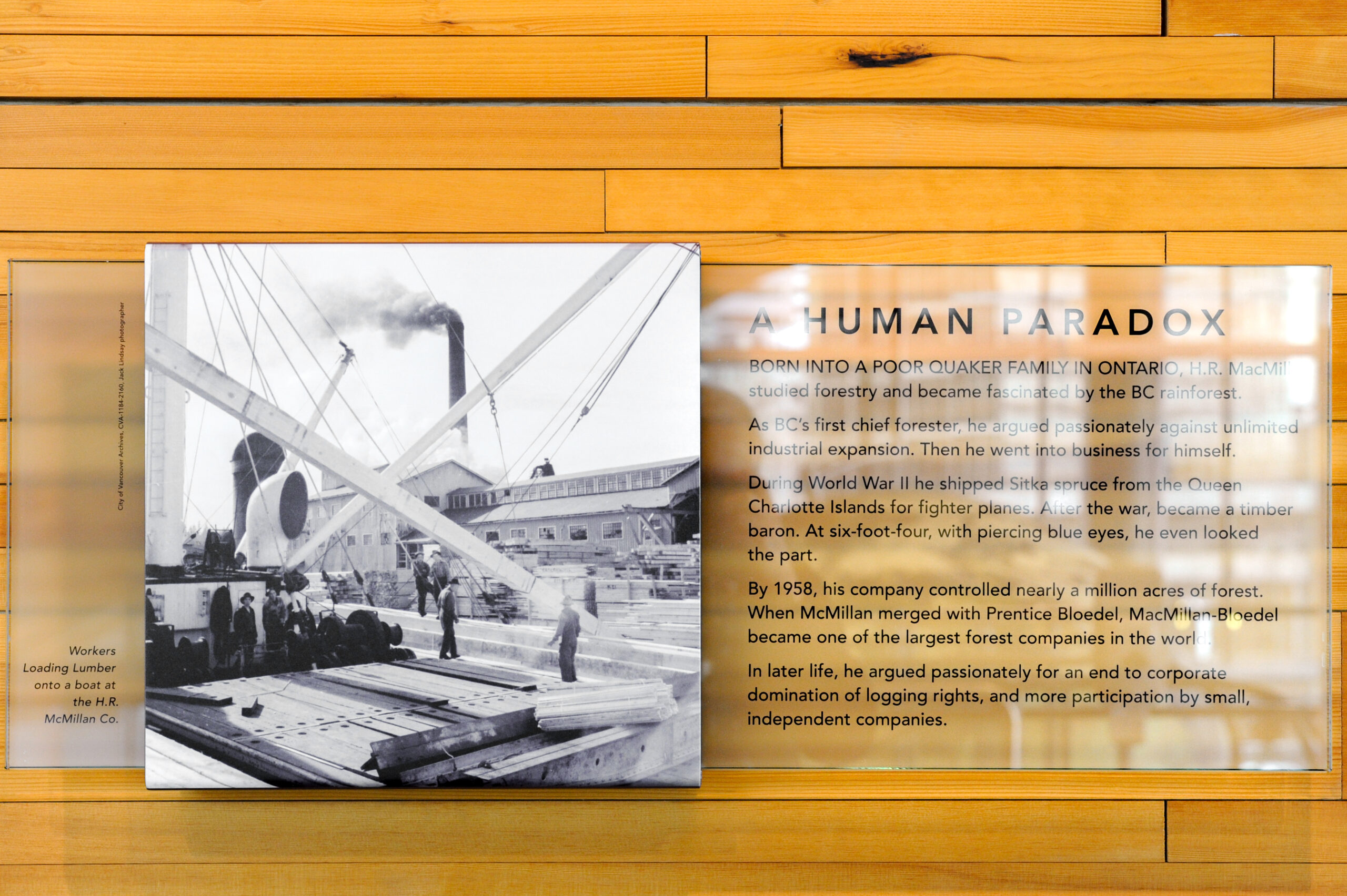 The plaque reads: Born into a poor Quaker family in Ontario, H.R. MacMillan studied forestry and became fascinated by the BC rainforest. As BC's first chief forester, he argued passionately against unlimited industrial expansion. Then he went into business for himself. During World War II, he shipped Sitka spruce from the Queen Charlotte Islands for fighter planes. After the war, he became a timber baron. At six-foot-four, with piercing blue eyes, he even looked the part. By 1958, his company controlled nearly a million acres of forest. When Macmillan merged with Prentice Bloedel, MacMillan Bloedel became one of the largest forest companies in the world. In later life, he argued passionately for an end to corporate domination of logging rights, and more participation by small, independent companies.