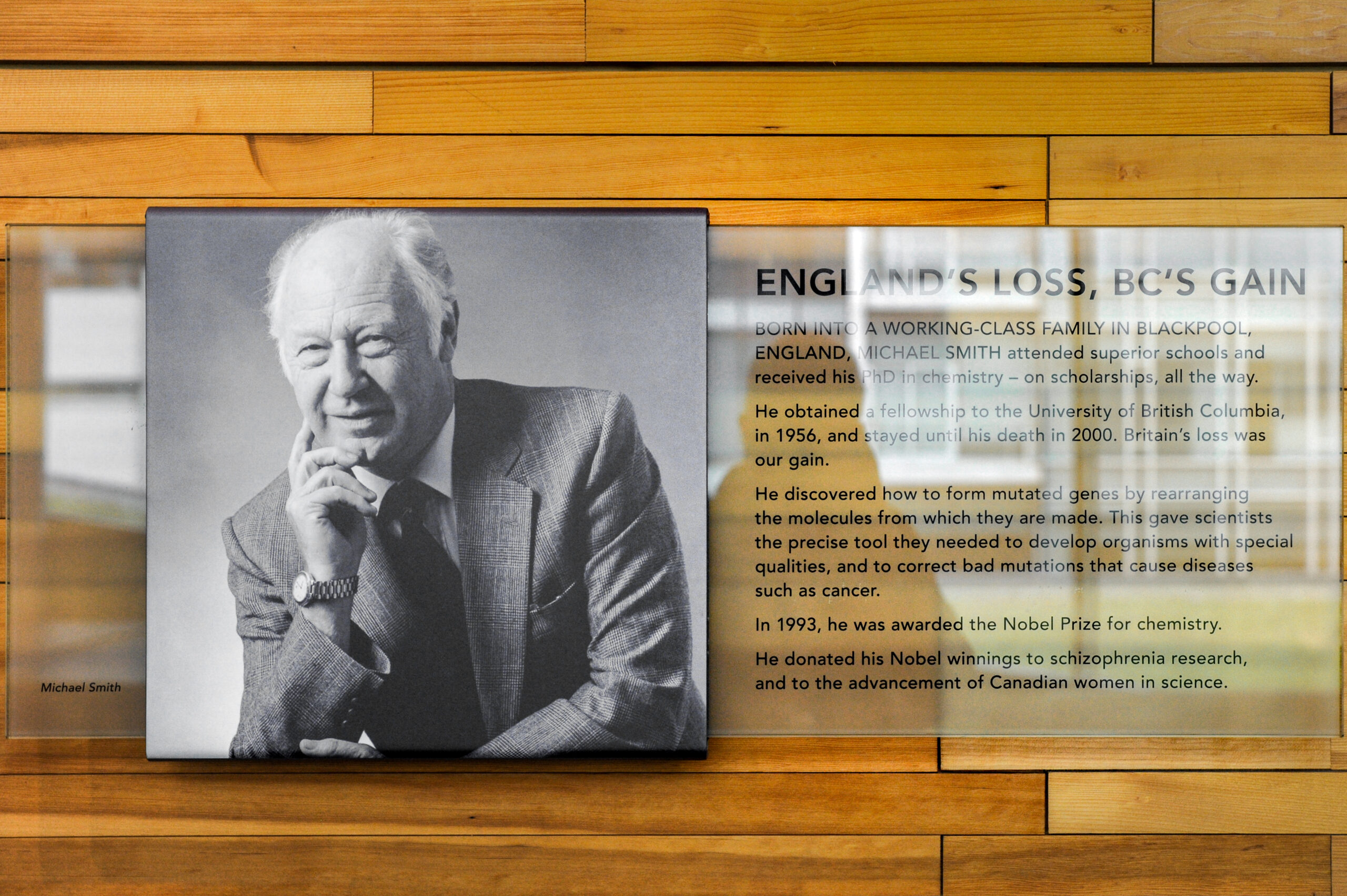 The plaque reads: Born into a working-class family in Blackpool, England, Michael Smith attended superior schools and received his PhD in chemistry — on scholarships, all the way. He obtained a fellowship to the University of British Columbia in 1956, and stayed until his death in 2000. Britain's loss was our gain. He discovered how to form mutated genes by rearranging the molecules from which they are made. This gave scientists the precise tools they needed to develop organisms with special qualities, and to correct bad mutations that cause diseases such as cancer. In 1993, he was awarded the Nobel Peace Prize for Chemistry. He donated his Nobel winnings to schizophrenia research, and to the advancement of Canadian women in science.