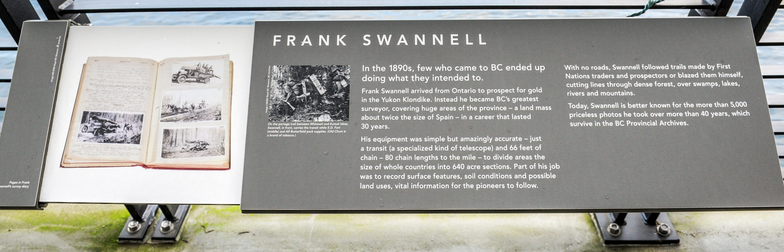 The plaque reads: In the 1890s, few who came to BC ended up doing what they intended to. Frank Swannell arrived from Ontario to prospect for gold in the Yukon Klondike. Instead he became BC’s greatest surveyor, covering huge areas of the province – a land mass about twice the size of Spain – in a career that lasted 30 years. His equipment was simple but amazingly accurate – just a transit (a specialized kind of telescope) and 66 feet of chain – 80 chain lengths to the mile – to divide areas the size of whole countries into 640 acre sections. Part of his job was to record surface features, soil conditions and possible land uses, vital information for the pioneers to follow. With no roads, Swannell followed trails made by First Nations traders and prospectors or blazed them himself, cutting lines through dense forest, over swamps, lakes, rivers and mountains. Today, Swannell is better known for the more than 5,000 priceless photos he took over more than 40 years, which survive in the BC Provincial Archives.