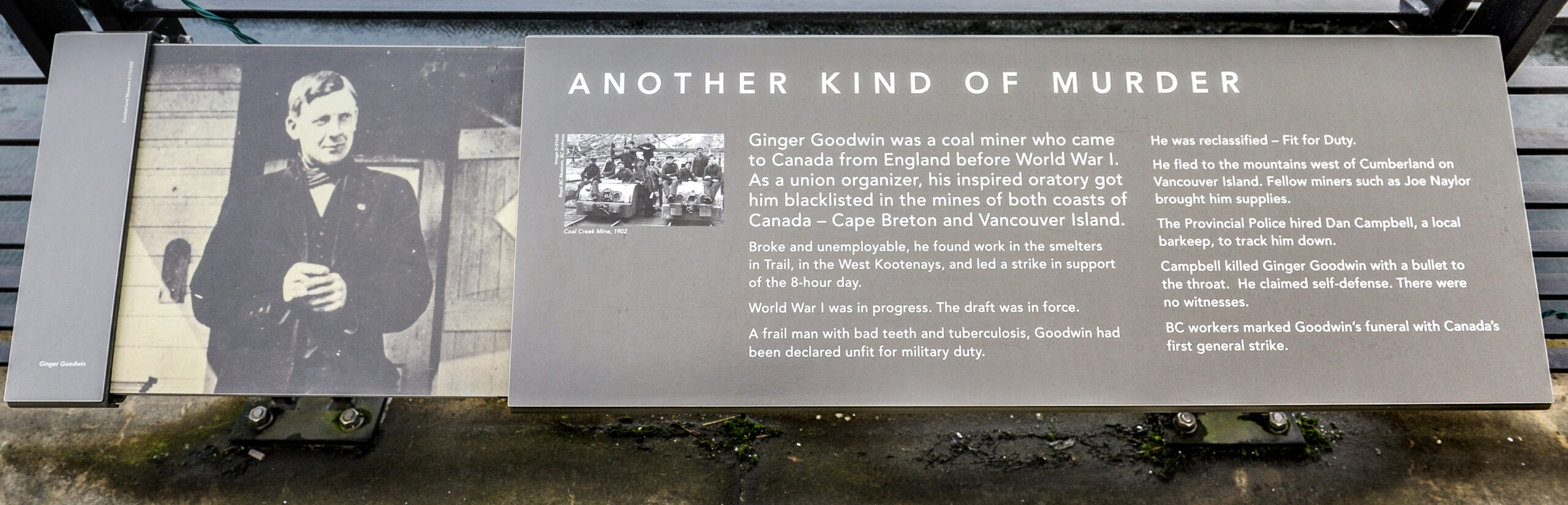 The plaque reads: Ginger Goodwin was a coal miner who came to Canada from England before World War I. As a union organizer, his inspired oratory got him blacklisted in the mines of both coasts of Canada – Cape Breton and Vancouver Island. Broke and unemployable, he found work in the smelters in Trail, in the West Kootenays, and led a strike in support of the 8-hour day. World War I was in progress. The draft was in force. A frail man with bad teeth and tuberculosis, Goodwin had been declared unfit for military duty. He was reclassified – Fit for Duty. He fled to the mountains west of Cumberland on Vancouver Island. Fellow miners such as Joe Naylor brought him supplies. The Provincial Police hired Dan Campbell, a local barkeep, to track him down. Campbell killed Ginger Goodwin with a bullet to the throat. He claimed self-defence. There were no witnesses. BC workers marked Goodwin’s funeral with Canada’s first general strike.