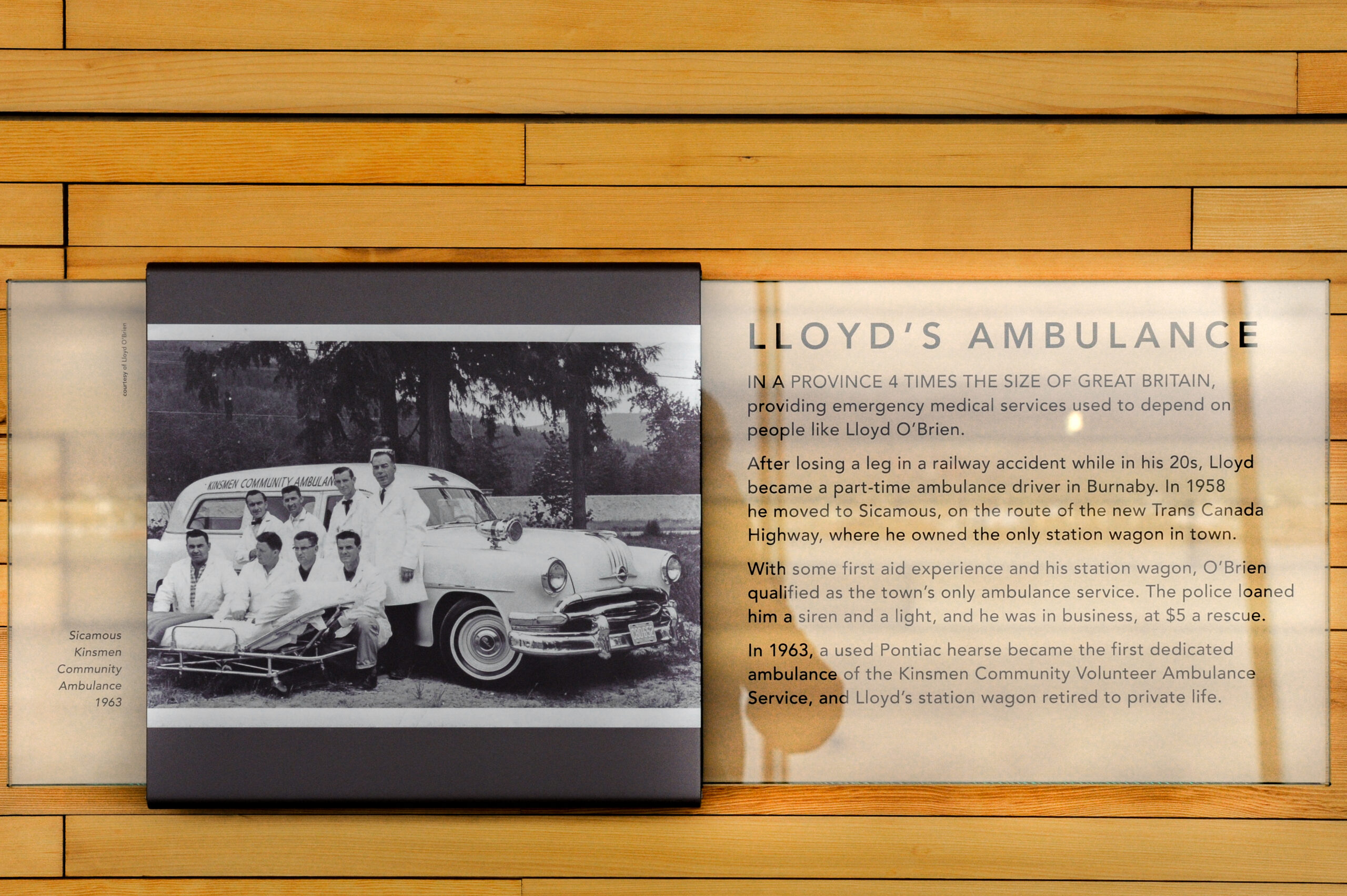 The plaque reads: In a province four times the size of Great Britain, providing emergency medical services used to depend on people like Lloyd O'Brien. After losing a leg in a railway accident while in his twenties, Lloyd became a part-time ambulance driver in Burnaby. In 1958 he moved to Sicamous, on the route of the new Trans-Canada Highway, where he owned the only station wagon in town. With some first aid experience and his station wagon, O'Brien qualified as the town's only ambulance service. The police loaned him a siren and a light, and he was in business, at $5 a rescue. In 1963, a used Pontiac Hearse became the first dedicated ambulance of the Kinsman Community Volunteer Ambulance Service, and Lloyd's station wagon retired to private life.