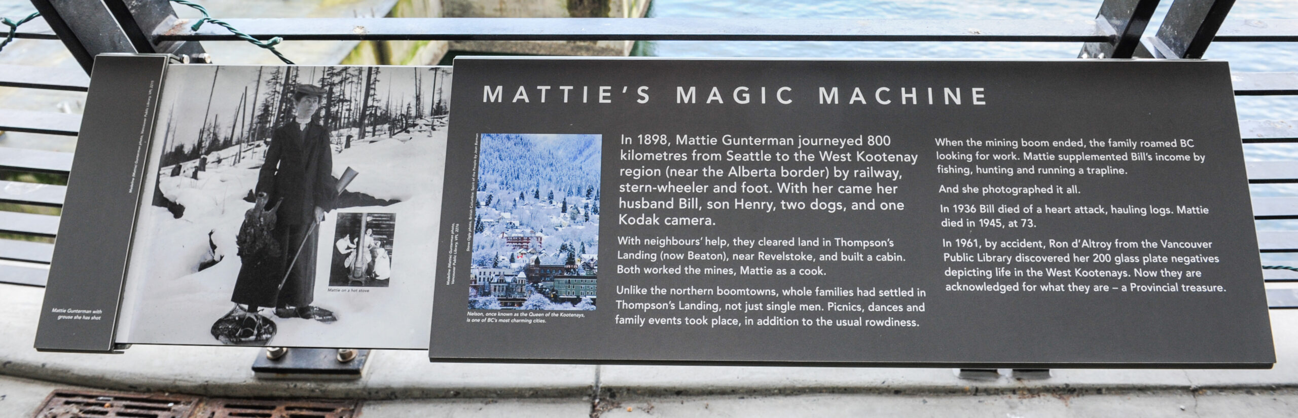 The plaque reads: In 1898, Mattie Gunterman journeyed 800 kilometres from Seattle to the West Kootenay region (near the Alberta border) by railway, stern-wheeler and foot. With her came her husband Bill, son Henry, two dogs, and one Kodak camera. With neighbours’ help, they cleared land in Thompson’s Landing (now Beaton), near Revelstoke, and built a cabin. Both worked the mines, Mattie as a cook. Unlike the northern boomtowns, whole families had settled in Thompson’s Landing, not just single men. Picnics, dances and family events took place, in addition to the usual rowdiness. When the mining boom ended, the family roamed BC looking for work. Mattie supplemented Bill’s income by fishing, hunting and running a trapline. And she photographed it all. In 1936 Bill died of a heart attack, hauling logs. Mattie died in 1945, at 73. In 1961, by accident, Ron d’Altroy from the Vancouver Public Library discovered her 200 glass plate negatives depicting life in the West Kootenays. Now they are acknowledged for what they are – a Provincial treasure.