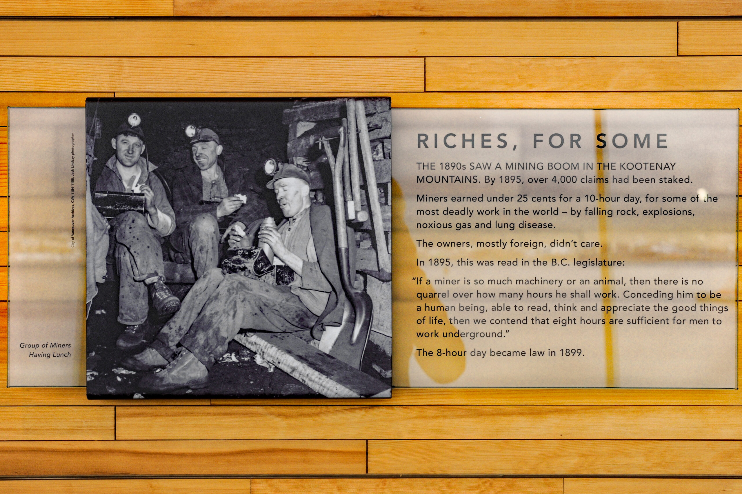 The plaque reads: The 1890s saw a mining boom in the Kootenay Mountains. By 1895, over 4,000 claims had been staked. Miners earned under 25 cents for a 10-hour day, for some of the most deadly work in the world — by falling rock explosions, noxious gas, and lung disease. The owners, mostly foreign, didn't care. In 1895, this was read in the BC Legislature: “If a miner is so much machinery or an animal, then there is no quarrel over how many hours he shall work. Conceding him to be a human being, able to read, think, and appreciate the good things of life, then we contend that 8 hours are sufficient for men to work underground.” The 8-hour day became law in 1899.