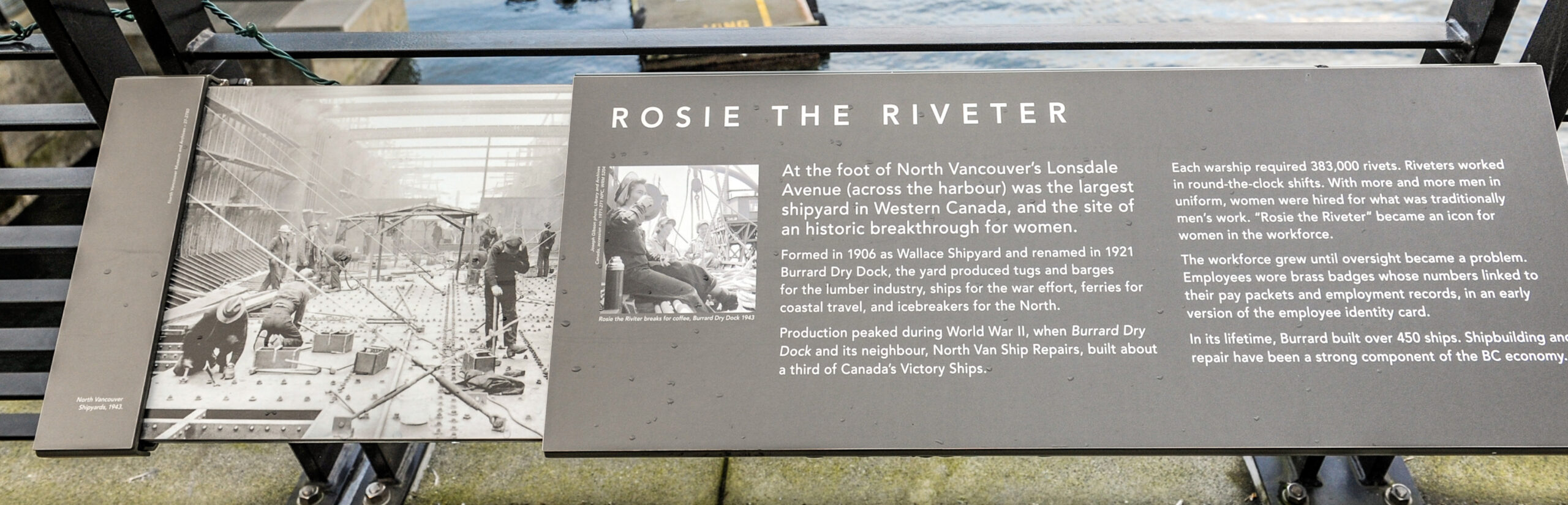 The plaque reads: At the foot of North Vancouver’s Lonsdale Avenue (across the harbour) was the largest shipyard in Western Canada, and the site of an historic breakthrough for women. Formed in 1906 as Wallace Shipyard and renamed in 1921 Burrard Dry Dock, the yard produced tugs and barges for the lumber industry, ships for the war effort, ferries for coastal travel, and icebreakers for the North. Production peaked during World War II, when Burrard Dry Dock and its neighbour, North Van Ship Repairs, built about a third of Canada’s Victory Ships. Each warship required 383,000 rivets. Riveters worked in round-the-clock shifts. With more and more men in uniform, women were hired for what was traditionally men’s work. “Rosie the Riveter” became an icon for women in the workforce. The workforce grew until oversight became a problem. Employees were issued badges whose numbers linked to their pay packets and employment records, in an early version of the employee identity card. In its lifetime, Burrard built over 450 ships. Shipbuilding and repair have been a strong component of the BC economy.