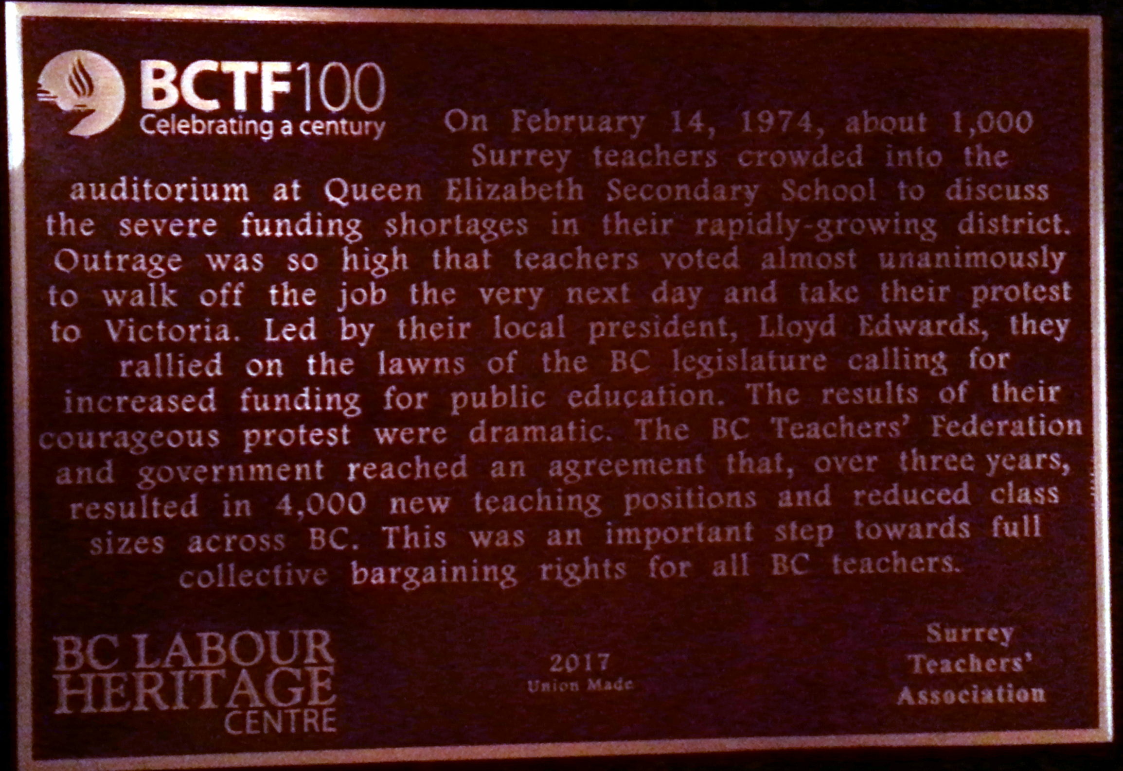 The plaque reads: On February 14, 1974, about 1,000 Surrey teachers crowded into the auditorium at Queen Elizabeth Secondary School to discuss the severe funding shortages in their rapidly-growing district. Outrage was so high that teachers voted almost unanimously to walk off the job the very next day and take their protest to Victoria. Led by their local president, Lloyd Edwards, they rallied on the lawns of the BC legislature calling for increased funding for public education. The results of their courageous protest were dramatic. The BC Teachers’ Federation and government reached an agreement that, over three years, resulted in 4,000 new teaching positions and reduced class sizes across BC. This was an important step towards full collective bargaining rights for all BC teachers. BC Labour Heritage Centre 2017 Union Made Surrey Teachers’ Association