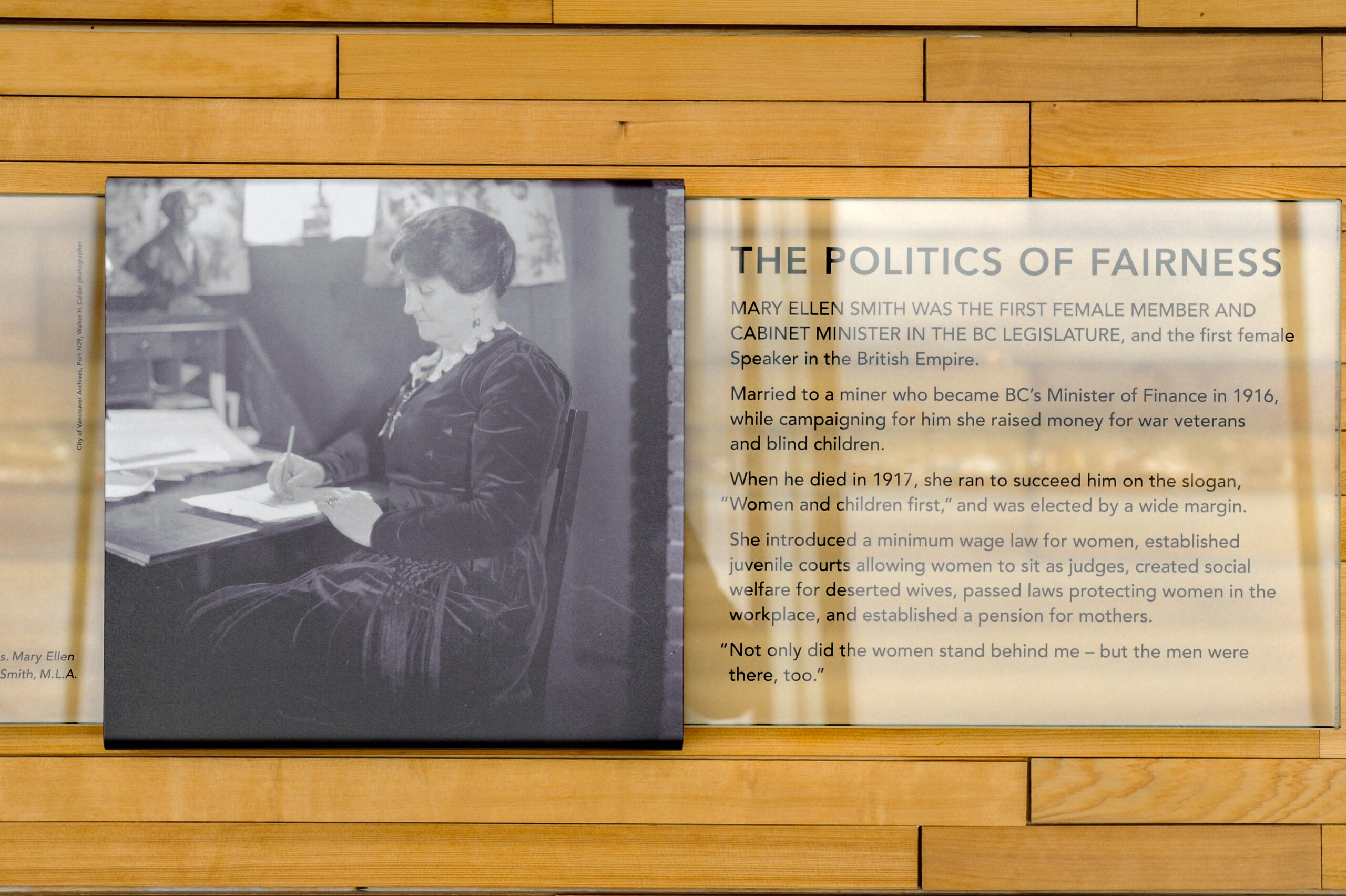 The plaque reads: Mary Ellen Smith was the first female member and Cabinet Minister of the B.C. Legislature, the first female Speaker in the British Empire. Married to a minor who became B.C.'s Minister of Finance in 1916, while campaigning for him she raised money for war veterans and blind children. When he died in 1917, she ran to succeed him on the slogan, “Women and Children First,” and was elected by a wide margin. She introduced a minimum wage law for women, established juvenile courts allowing women to sit as judges, created social welfare for deserted wives, passed laws protecting women in the workplace, and established a pension for mothers. “Not only did the women stand behind me — but the men were there too.”
