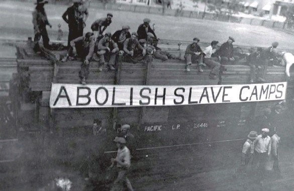 A group of men on and around a railway car with a banner across that says: abolish slave camps"