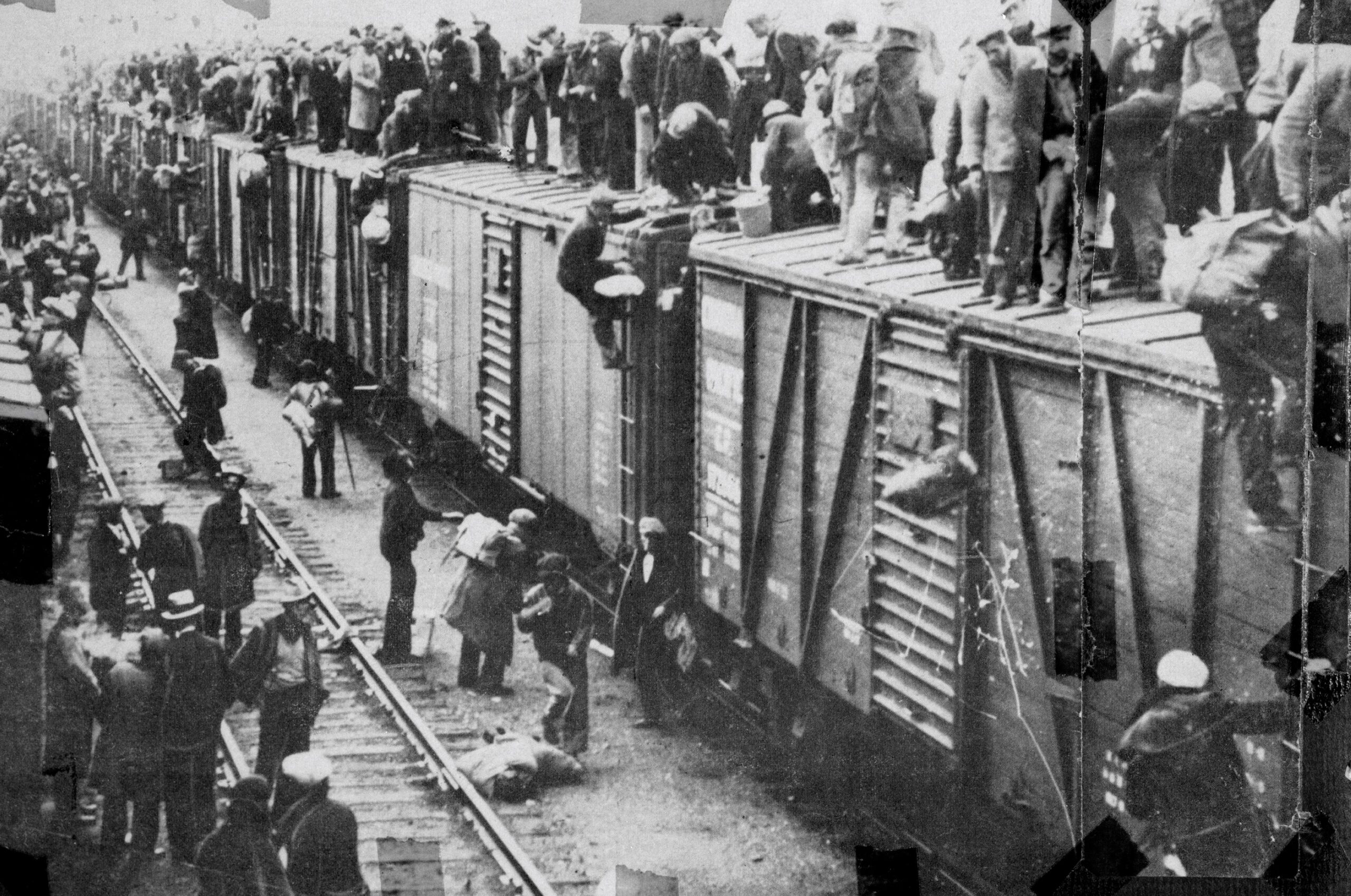 Black and white photo of a group of men boarding and sitting on top of a train