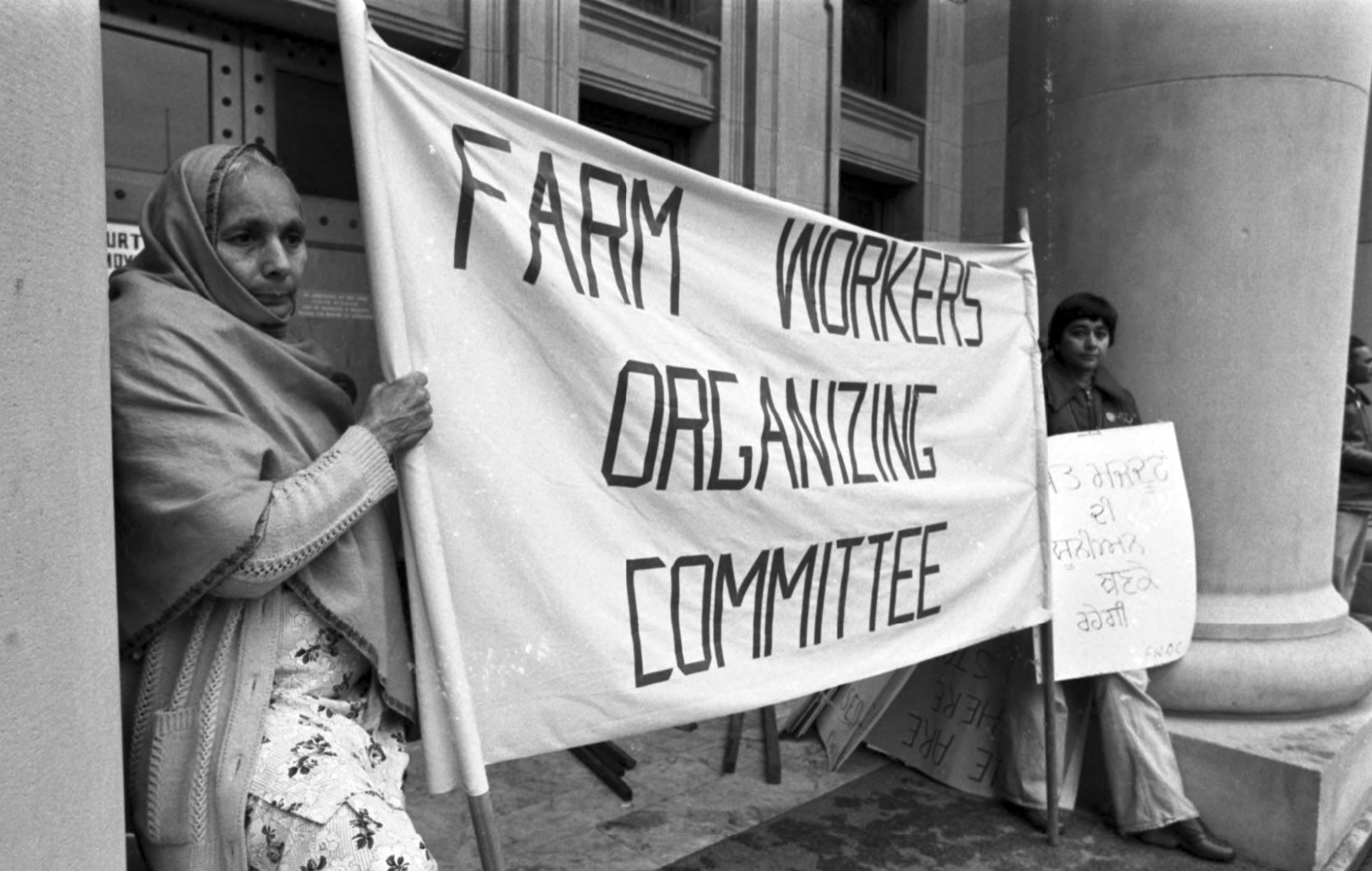 Two farm working women holding up a large banner that reads: Farm workers organizing committee