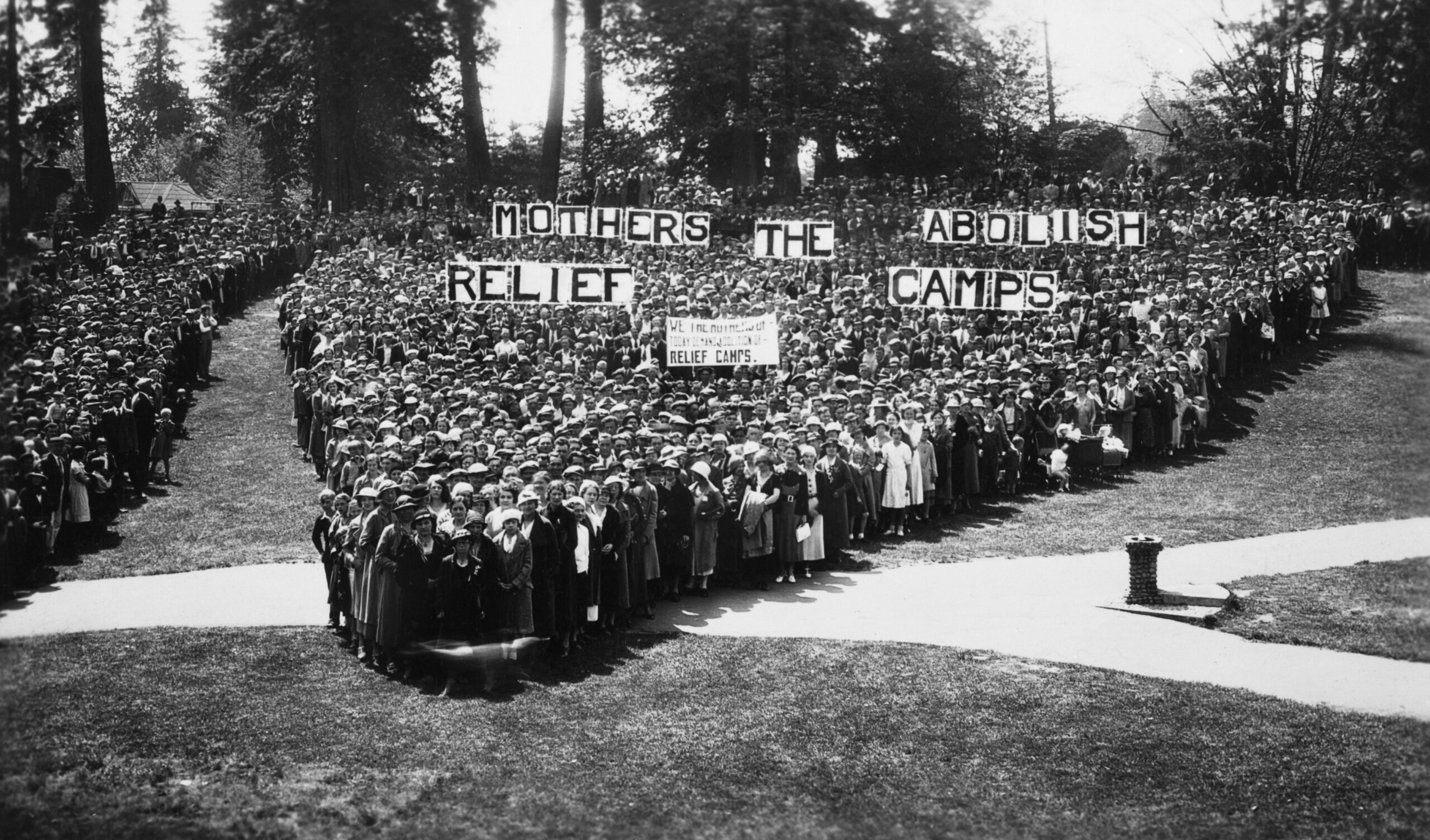 Black and white photo of a large group of protesting women, holding up a sign that says "Mothers Relief Abolish The Camps